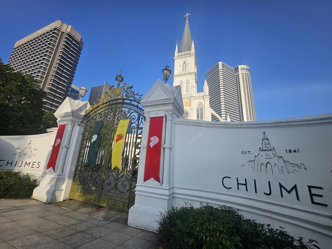 CHIJMES' 1841 gate dressed in National Day banners, with the chapel spire and Carlton tower behind
