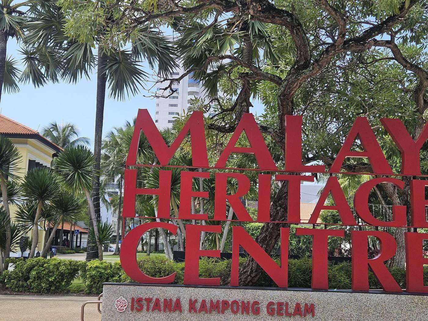 Malay Heritage Centre lettering framed by frangipani and palms at Istana Kampong Gelam